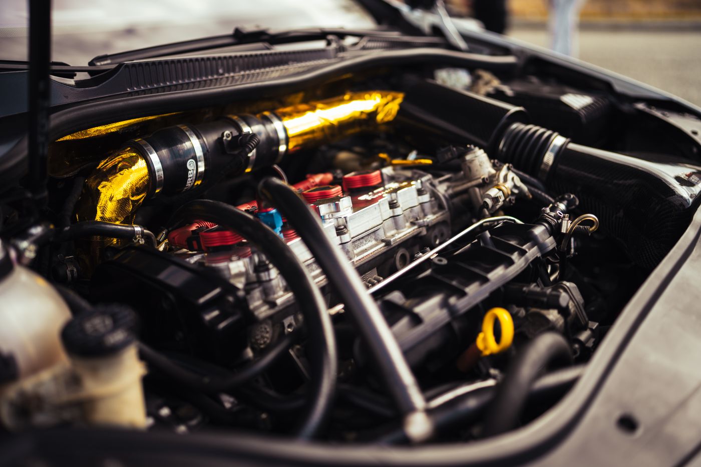 Car engine compartment with a gold heat-wrap sleeve around an air intake pipe and black hoses