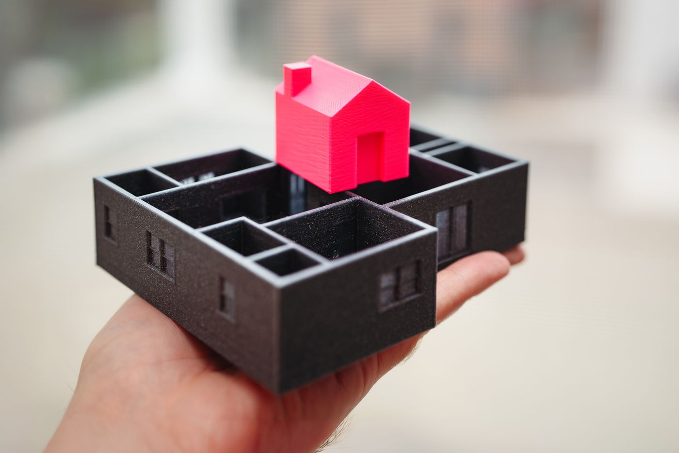 Hand holding a 3D-printed architectural model of a house on a floor plan
