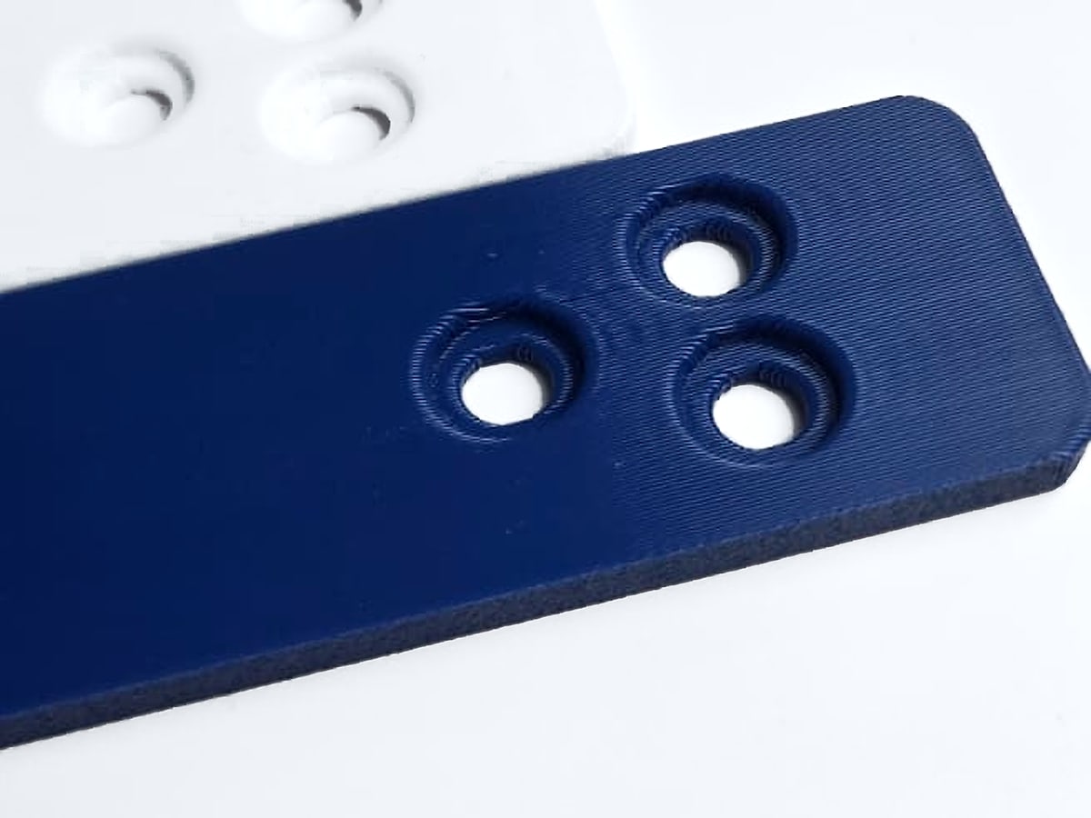 Close-up of blue and white 3D-printed plates with three countersunk holes each